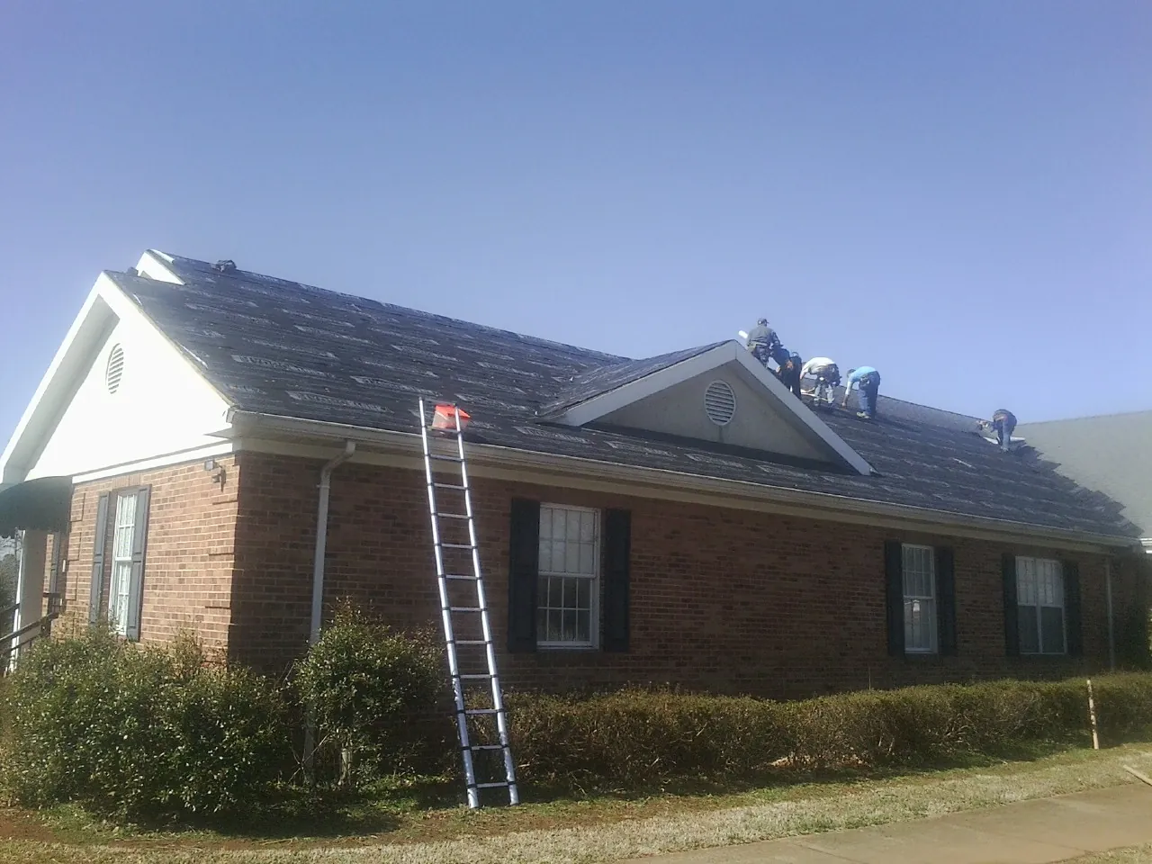Crew tearing shingles off a brick ranch roof with a ladder set — Emergency Roof Repair work by our crew in Lawtey