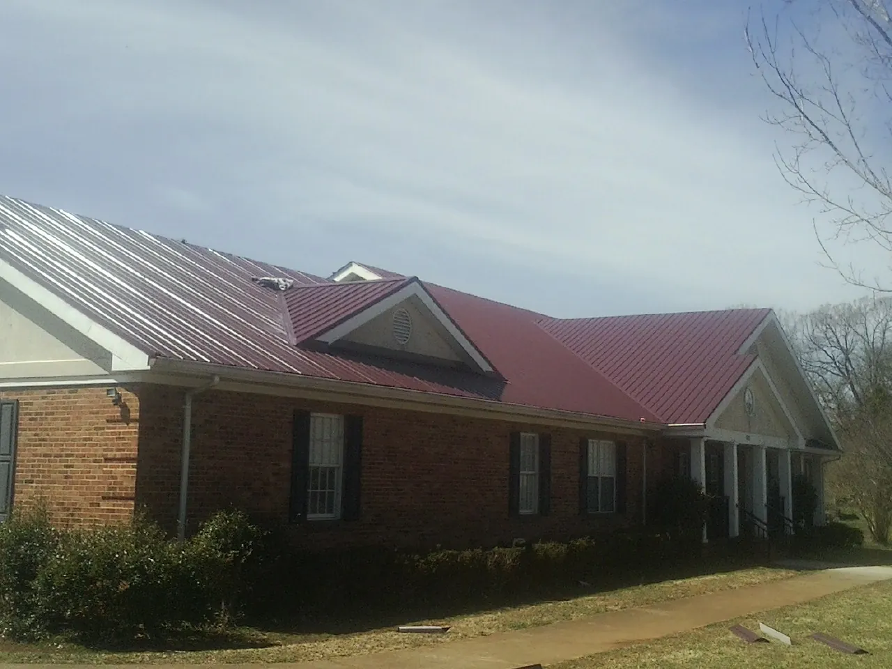 Red metal roof with gabled entries on a long brick building, from a Hail Damage Roof Repair job in Lawtey