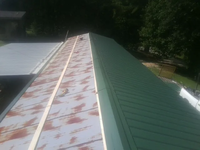 Old rusted panels beside newly installed green metal roofing — Wind Damage Roof Repair by Roofing Brothers in Lawtey