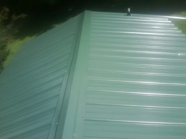 New green metal panels meeting at the ridge of a roof — Flat Roof Repair work by our crew in Lawtey