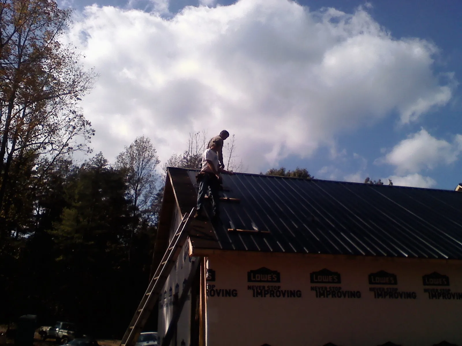 Roofer fastening dark metal panels high against a cloudy sky, from a Roof Inspection job in Lawtey