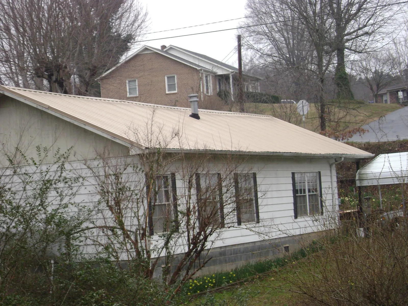 Tan metal roof on a white sided house set into a hillside — Commercial Roofing by Roofing Brothers in Lawtey